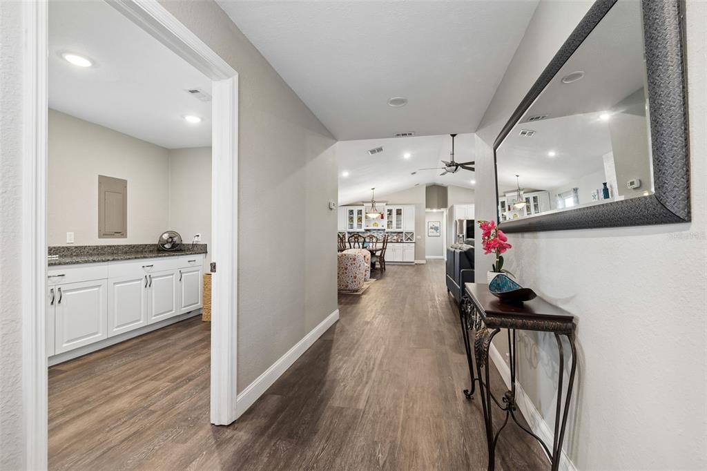A hallway with wood-look flooring leads to an open-concept kitchen and living area — 9901 BAY DRIVE, GIBSONTON, FL