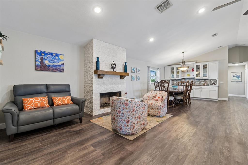 A living room with a stone fireplace, gray sofa, floral chairs, and an adjacent dining area — 9901 BAY DRIVE, GIBSONTON, FL