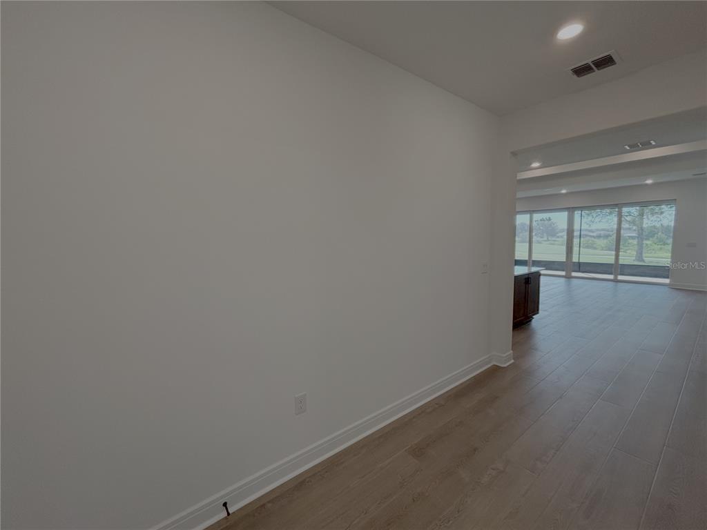 A large, empty white wall stands in a room with light wood-look flooring — 6360 SW 82 TERRACE, OCALA, FL