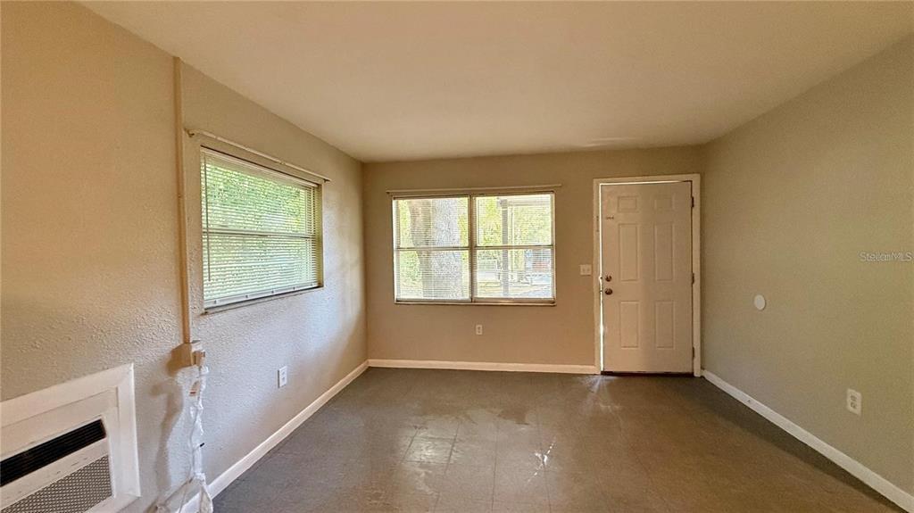 An empty room with beige walls, two windows, a white door, and gray flooring — 213 DR MARTIN LUTHER KING JR AVENUE, WILDWOOD, FL