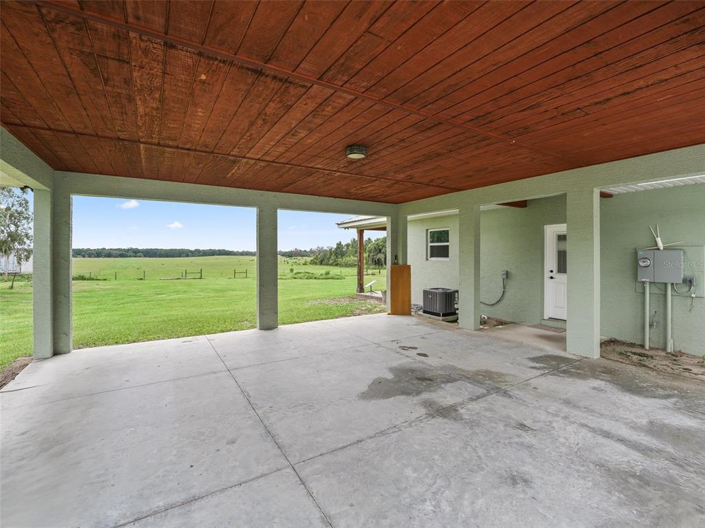 A covered concrete patio features a wood-paneled ceiling and overlooks a large, open grassy field — 8567 CR 635, BUSHNELL, FL