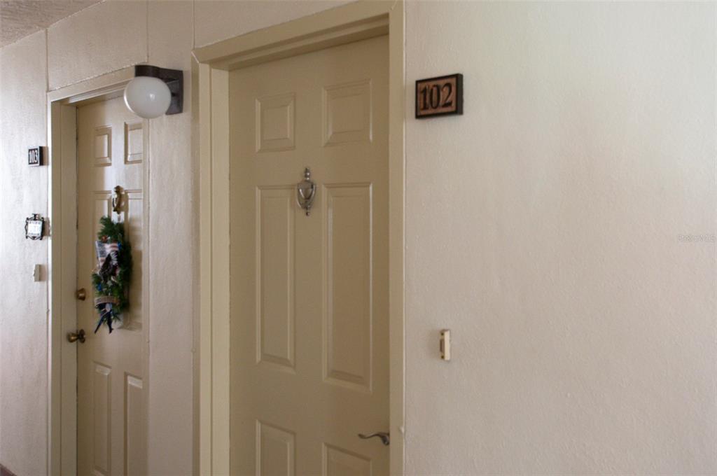 A hallway view showing two apartment doors numbered 102 and 103 with wall-mounted light fixtures — 7903 SAILBOAT KEY BOULEVARD S UNIT 102, SOUTH PASADENA, FL
