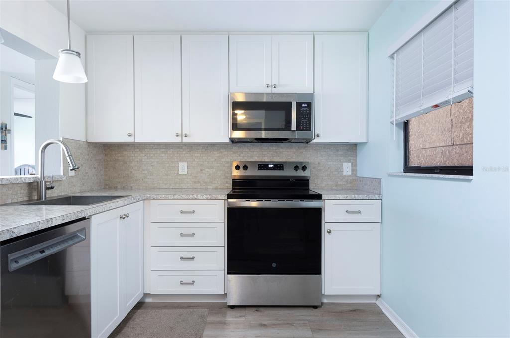 A kitchen features white cabinets, stainless steel appliances, a tiled backsplash, and light-colored countertops — 7903 SAILBOAT KEY BOULEVARD S UNIT 102, SOUTH PASADENA, FL