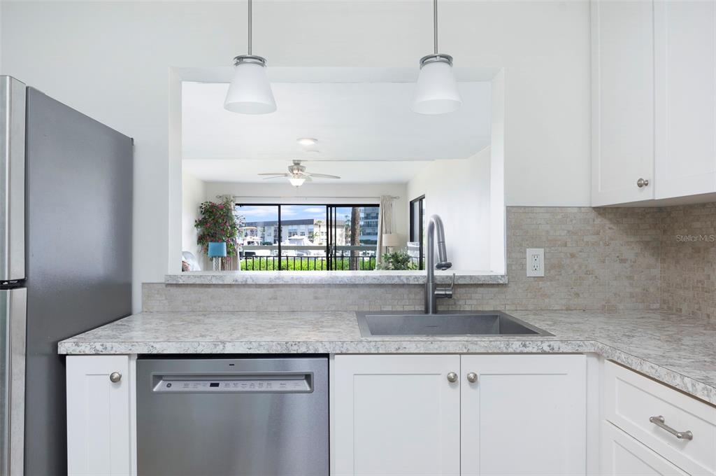 A kitchen features white cabinets, a stone-look countertop, stainless steel appliances, and a pass-through window — 7903 SAILBOAT KEY BOULEVARD S UNIT 102, SOUTH PASADENA, FL
