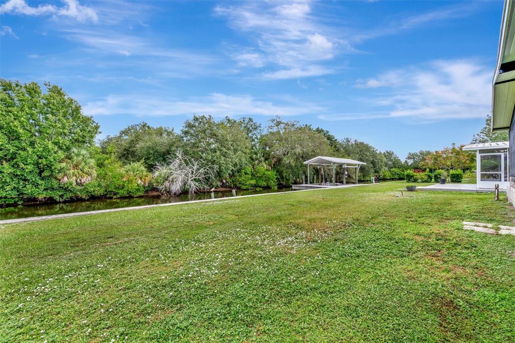 A grassy backyard features a concrete seawall, a boat lift, and dense trees along a canal — 236 N SAINT THOMAS CIRCLE, APOLLO BEACH, FL