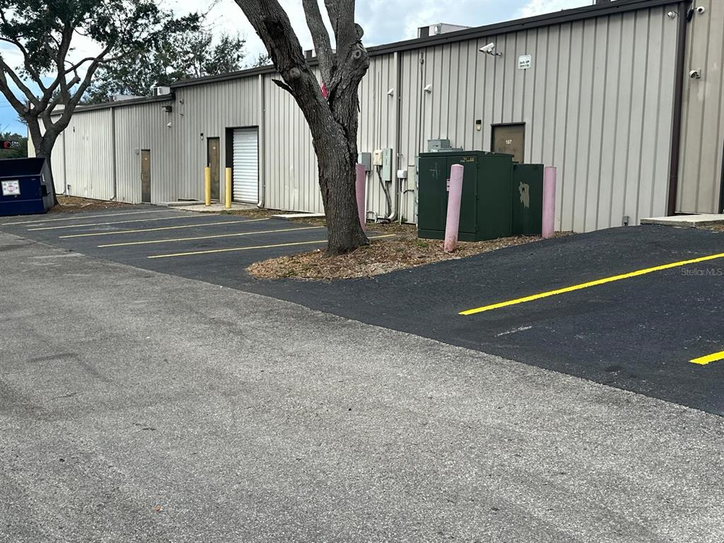 An exterior view of a metal warehouse building with parking spaces and a large tree — 1727 E BUSCH BOULEVARD, TAMPA, FL