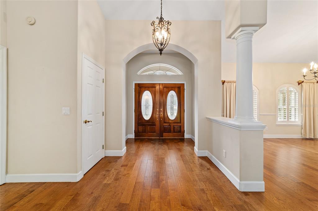 An entryway with hardwood floors, a white column, and double wooden front doors with glass — 7939 SE 12TH CIRCLE, OCALA, FL