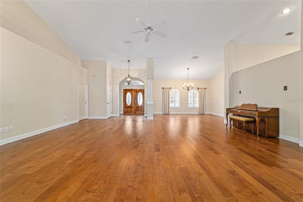 A spacious living room features hardwood floors, vaulted ceilings, a piano, and a double-door entrance — 7939 SE 12TH CIRCLE, OCALA, FL