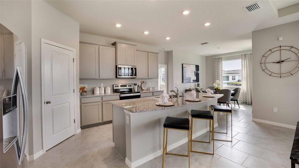 A modern kitchen features gray cabinets, granite countertops, a center island, and tile flooring — 32645 DULUTH DRIVE, WESLEY CHAPEL, FL