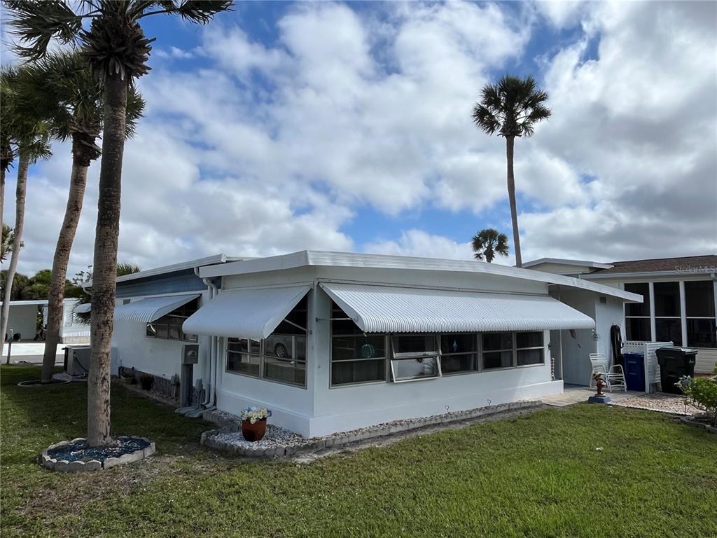 A white mobile home features metal awnings over its windows and several tall palm trees — 206 ROMA ROAD, VENICE, FL