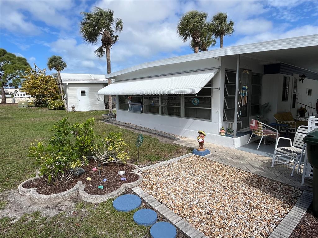 A mobile home exterior features a white awning, a gravel patio, and a landscaped garden — 206 ROMA ROAD, VENICE, FL