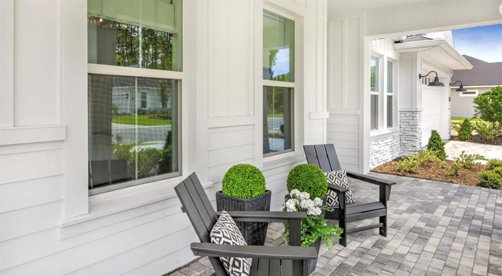 A covered front porch features two black chairs, potted plants, and white siding — 443 STIRLING BRIDGE DRIVE, ORMOND BEACH, FL