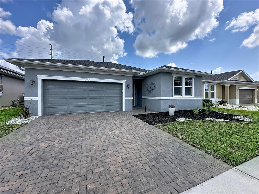 A gray single-story house features a paved driveway, a two-car garage, and landscaped front yard — 174 SILVER MAPLE ROAD, GROVELAND, FL