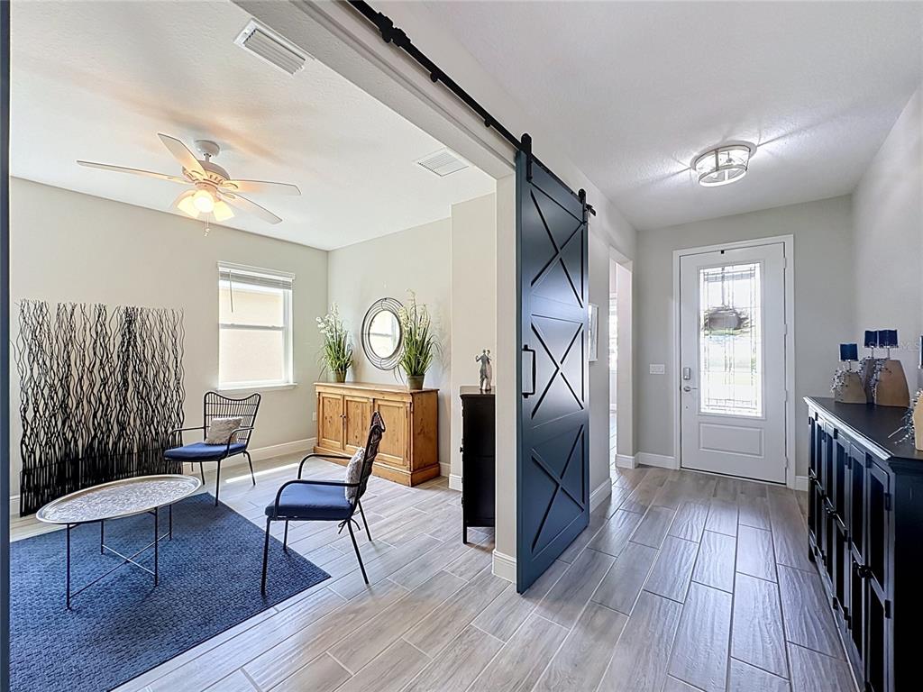 A foyer with tile flooring leads to a sitting room featuring a dark sliding barn door — 174 SILVER MAPLE ROAD, GROVELAND, FL