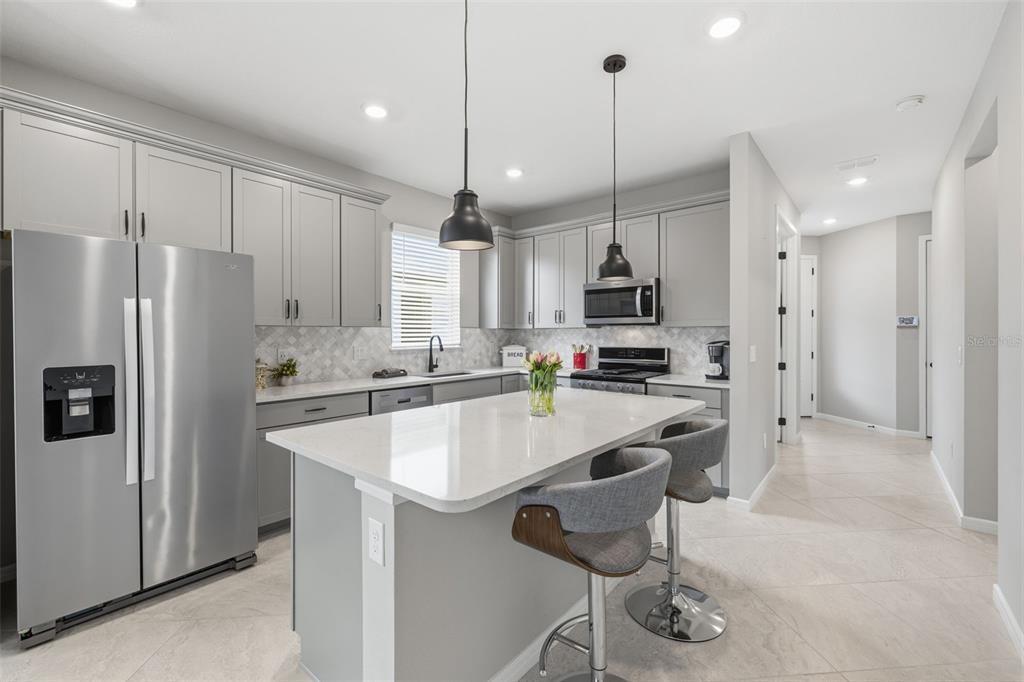 A modern kitchen features gray cabinets, stainless steel appliances, a white island, and tile flooring — 10462 SPRING TIDE WAY, PARRISH, FL