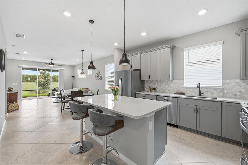 A modern kitchen features gray cabinets, a quartz island with bar stools, and tile flooring — 10462 SPRING TIDE WAY, PARRISH, FL