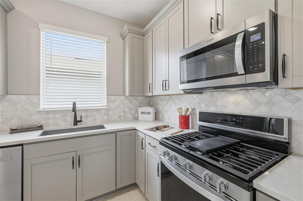 A kitchen features light gray cabinets, white countertops, a gas range, and a microwave — 10462 SPRING TIDE WAY, PARRISH, FL