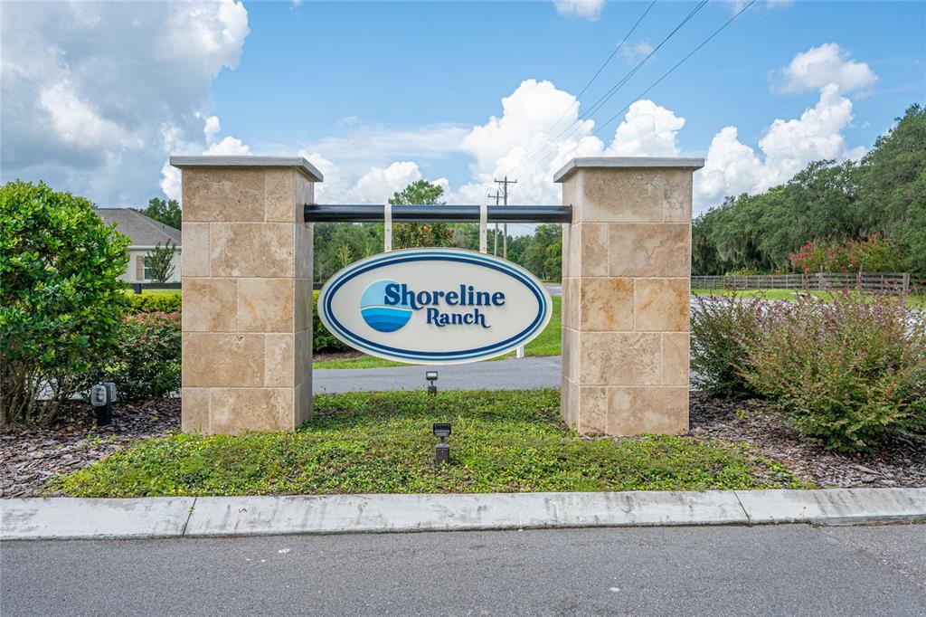 A stone monument sign for Shoreline Ranch stands in a landscaped area under a blue sky — 38345 LAKE MEADOW COURT, UMATILLA, FL