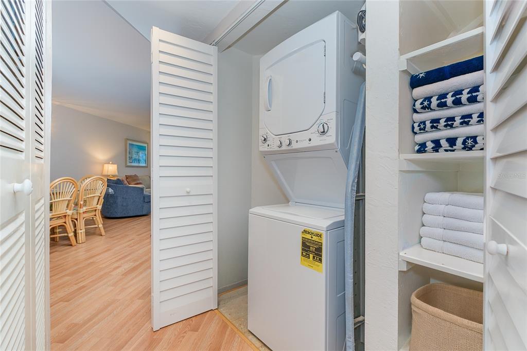 A laundry closet contains a stacked washer and dryer next to open shelving with towels — 7454 PLACIDA ROAD UNIT 3312, PLACIDA, FL