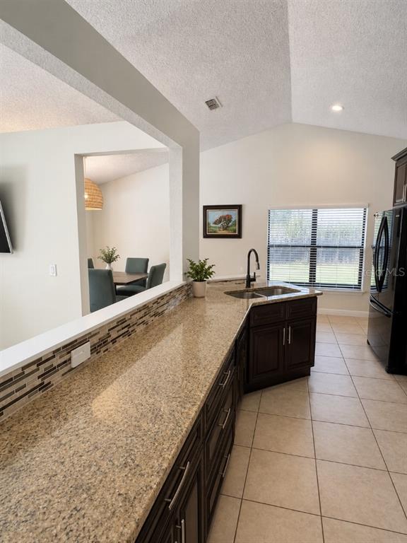 A kitchen with granite countertops, dark cabinets, and a pass-through window to the dining area — 1348 WINTERVILLE STREET, DELTONA, FL
