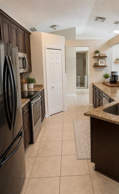 A kitchen with dark wood cabinets, granite countertops, stainless steel appliances, and beige tile flooring — 1348 WINTERVILLE STREET, DELTONA, FL
