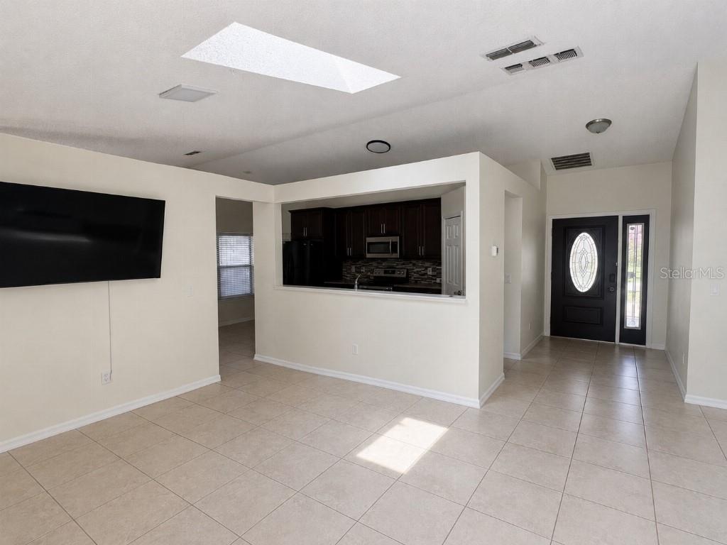 A living room with tile floors, a wall-mounted television, and a pass-through to the kitchen — 1348 WINTERVILLE STREET, DELTONA, FL