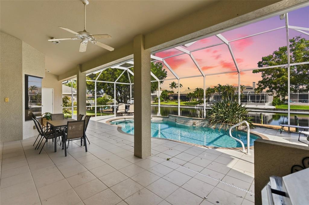 A covered patio features a dining set, ceiling fan, and a screened pool overlooking water — 1819 SW 47TH STREET, CAPE CORAL, FL