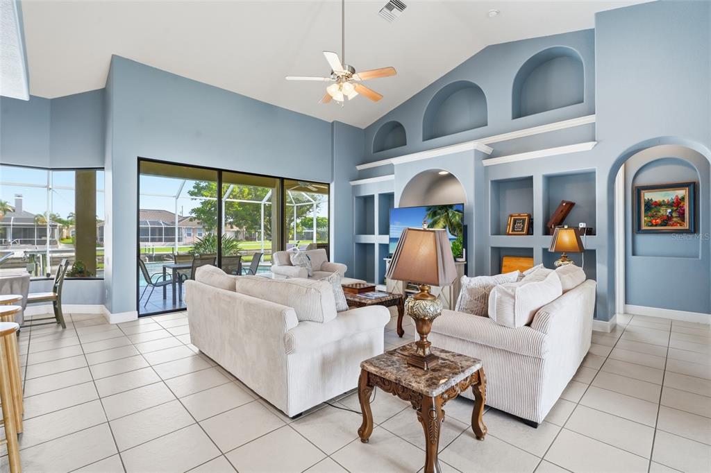 A living room with light blue walls, vaulted ceilings, tile floors, and a built-in entertainment center — 1819 SW 47TH STREET, CAPE CORAL, FL