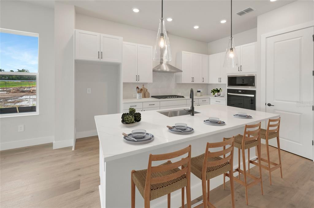 A modern kitchen features white cabinetry, a large quartz island, and light wood flooring — 6821 CHLOE COURT, SARASOTA, FL