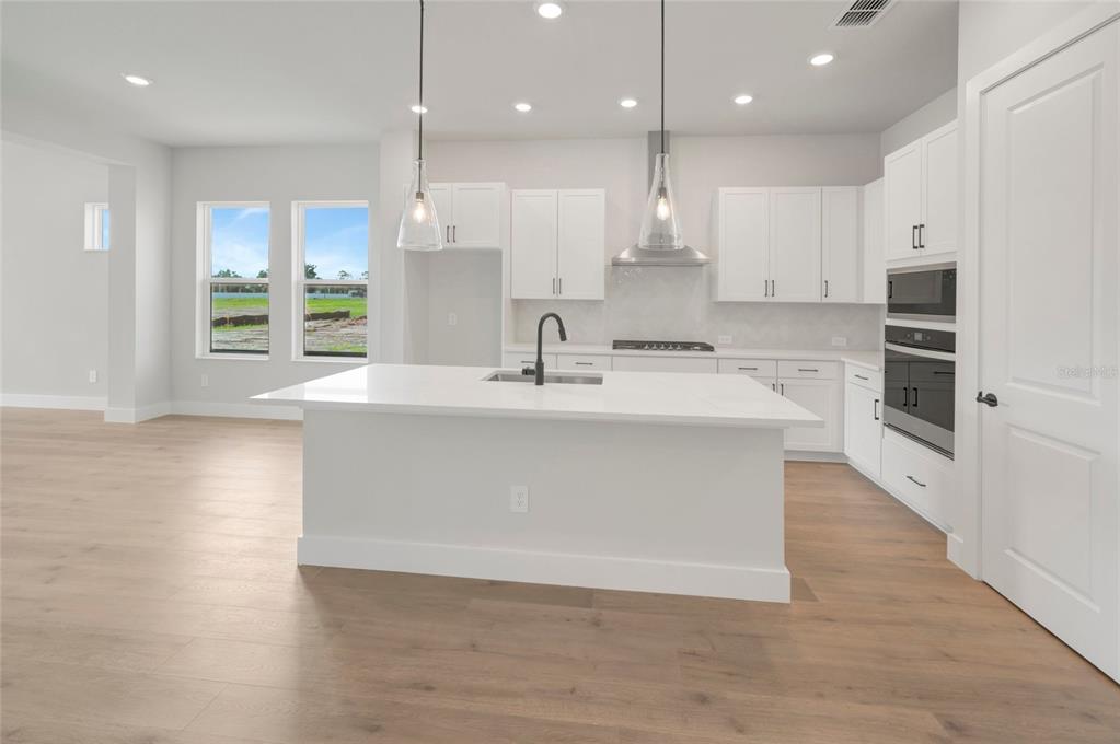 A modern white kitchen features a large center island, stainless steel appliances, and light flooring — 6821 CHLOE COURT, SARASOTA, FL