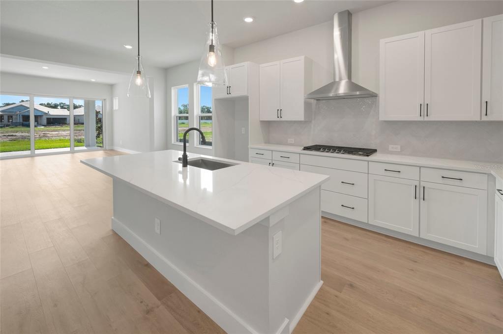 A modern kitchen features white cabinetry, a large quartz island, and light wood flooring — 6821 CHLOE COURT, SARASOTA, FL