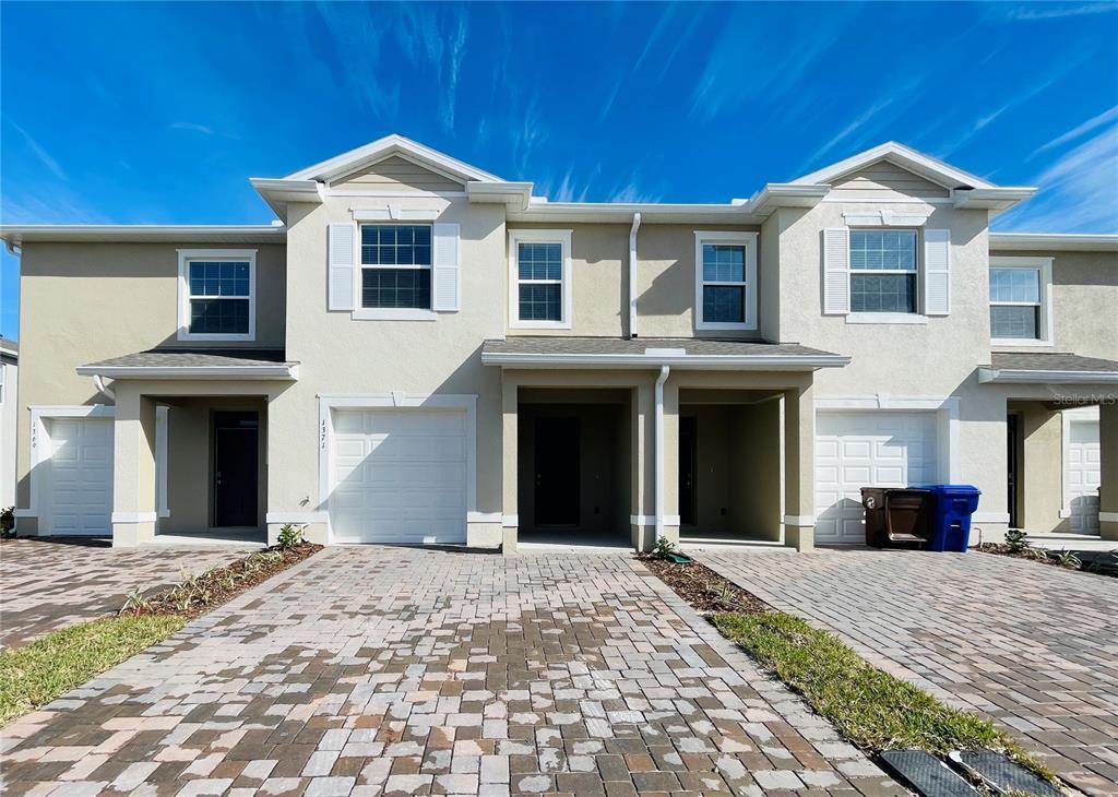 A row of multi-story townhomes with beige stucco facades, paver driveways, and attached garages — 1371 ISLETA LOOP, KISSIMMEE, FL