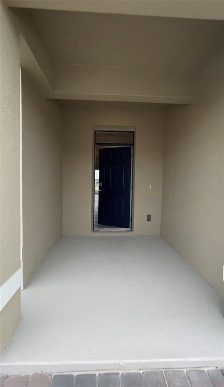 A covered entryway features beige walls, a concrete floor, and a dark blue front door — 1371 ISLETA LOOP, KISSIMMEE, FL