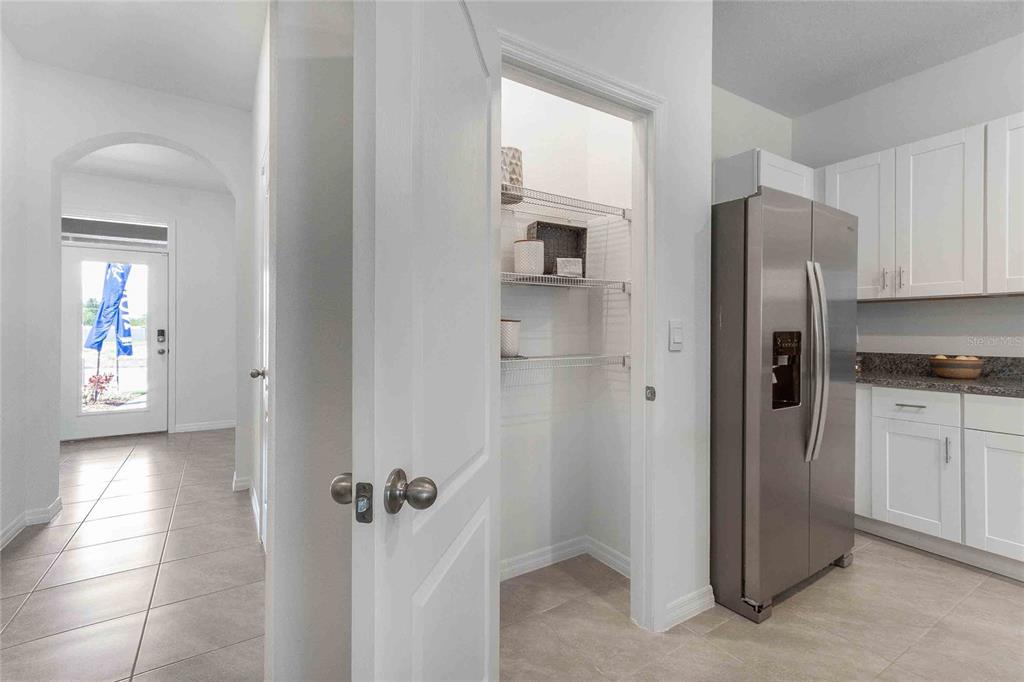A kitchen pantry with wire shelving is positioned between a hallway and a stainless refrigerator — 1371 ISLETA LOOP, KISSIMMEE, FL