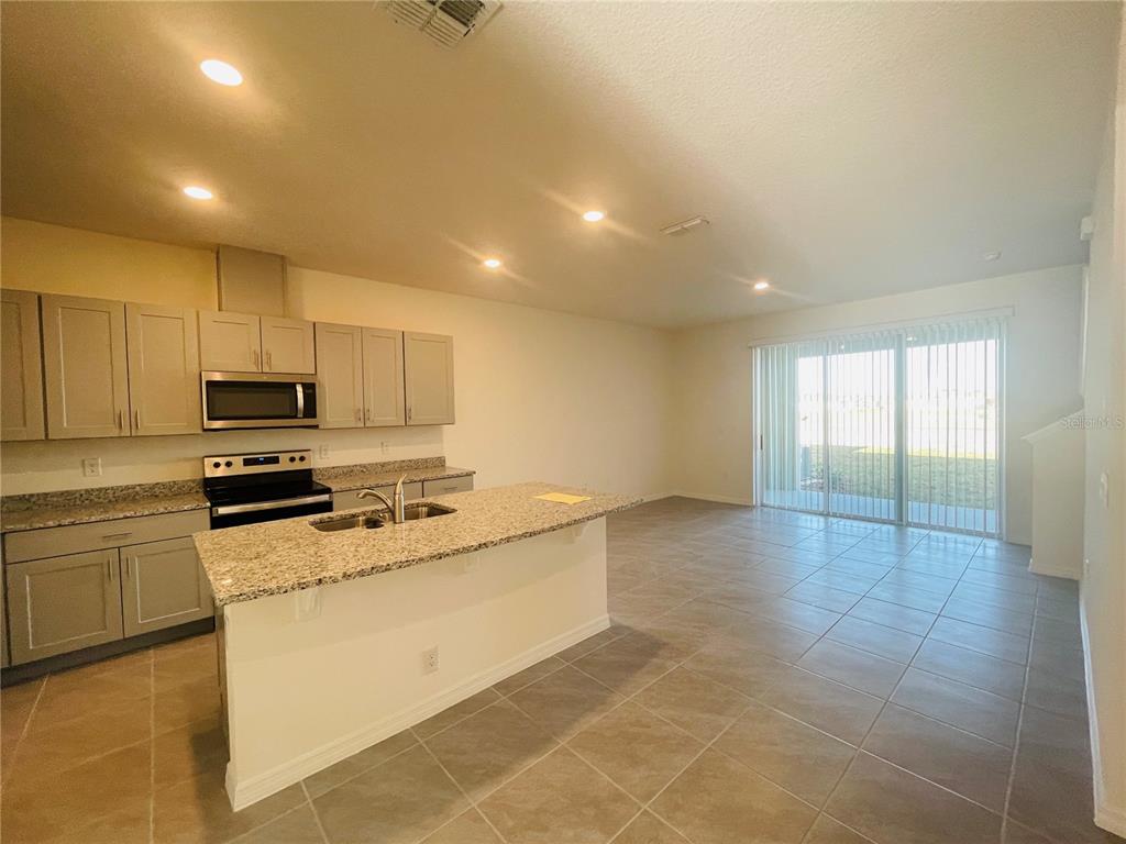 A kitchen with granite countertops and light-colored cabinets opens into a tiled living area — 1371 ISLETA LOOP, KISSIMMEE, FL