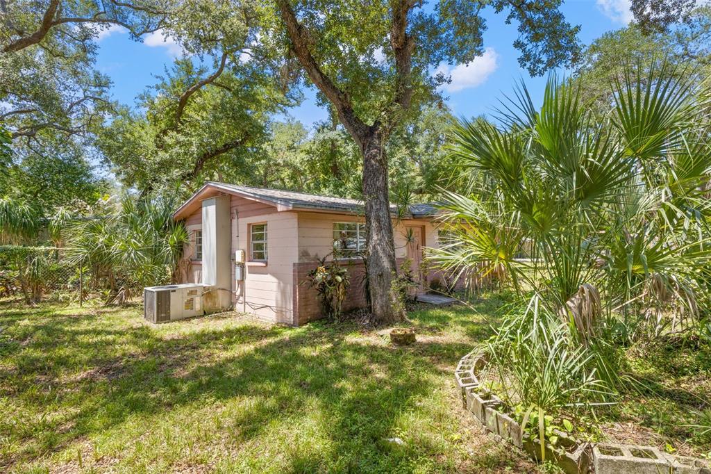 A small, single-story house with pink siding and a brick base sits in a wooded yard — 6903 OHIO AVENUE, GIBSONTON, FL