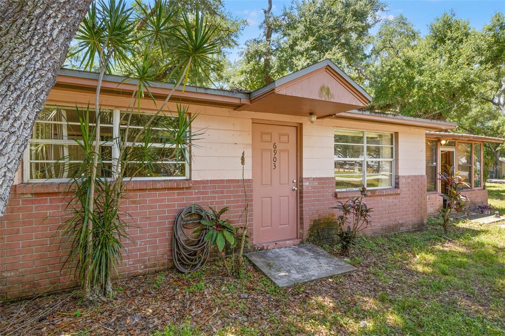 A single-story house exterior features a brick lower facade, pink upper walls, and a front door — 6903 OHIO AVENUE, GIBSONTON, FL