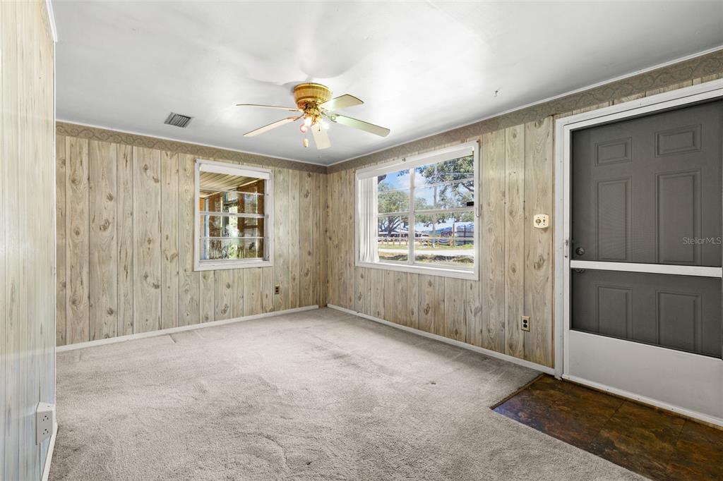 A room with wood-paneled walls, beige carpeting, a ceiling fan, and a gray exterior door — 6903 OHIO AVENUE, GIBSONTON, FL