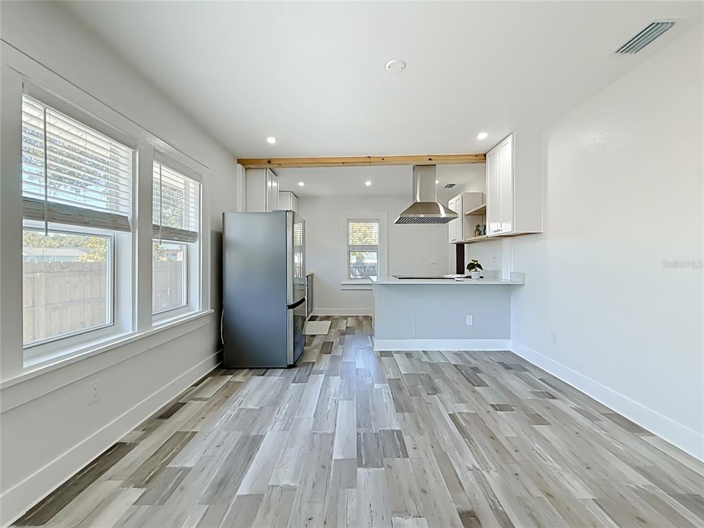 A kitchen and dining area feature gray wood-look flooring, white cabinets, and a stainless refrigerator — 1435 PRESCOTT STREET S, ST PETERSBURG, FL