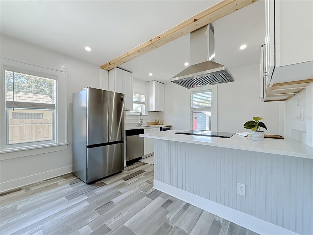 A modern kitchen features white cabinetry, stainless steel appliances, a breakfast bar, and wood-look flooring — 1435 PRESCOTT STREET S, ST PETERSBURG, FL