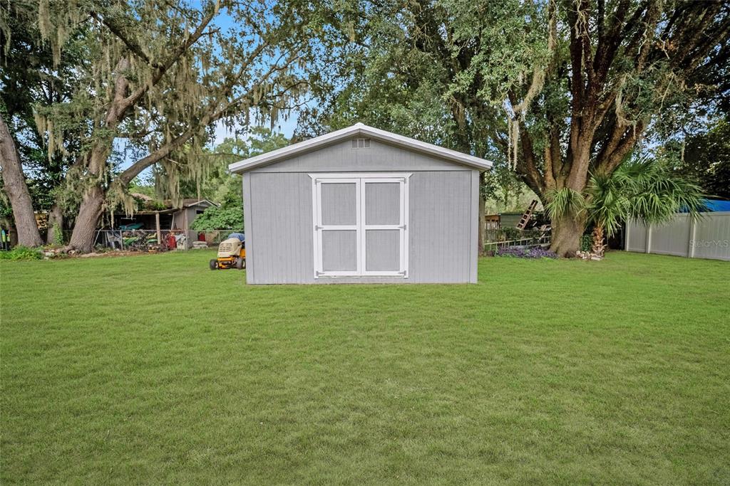 A gray storage shed with white-trimmed double doors sits in a grassy backyard — 9529 SW 30TH TERRACE, OCALA, FL