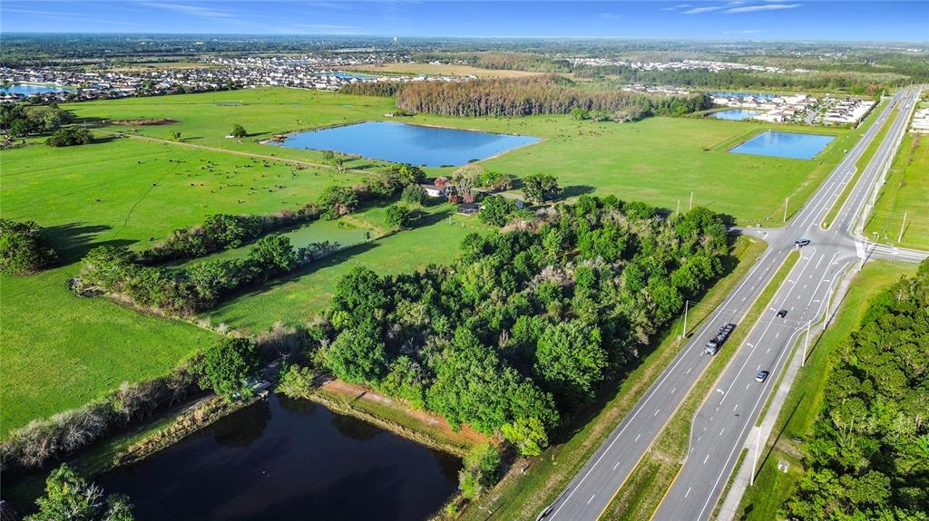 An aerial view shows a large grassy field with ponds, trees, and an adjacent highway — 0000 OLD HICKORY TREE ROAD, ST CLOUD, FL