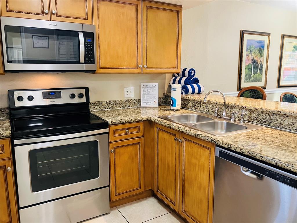 A kitchen with wooden cabinets, granite countertops, and stainless steel appliances including a microwave and stove — 1021 BASEBALL AND BOARDWALK COURT, KISSIMMEE, FL