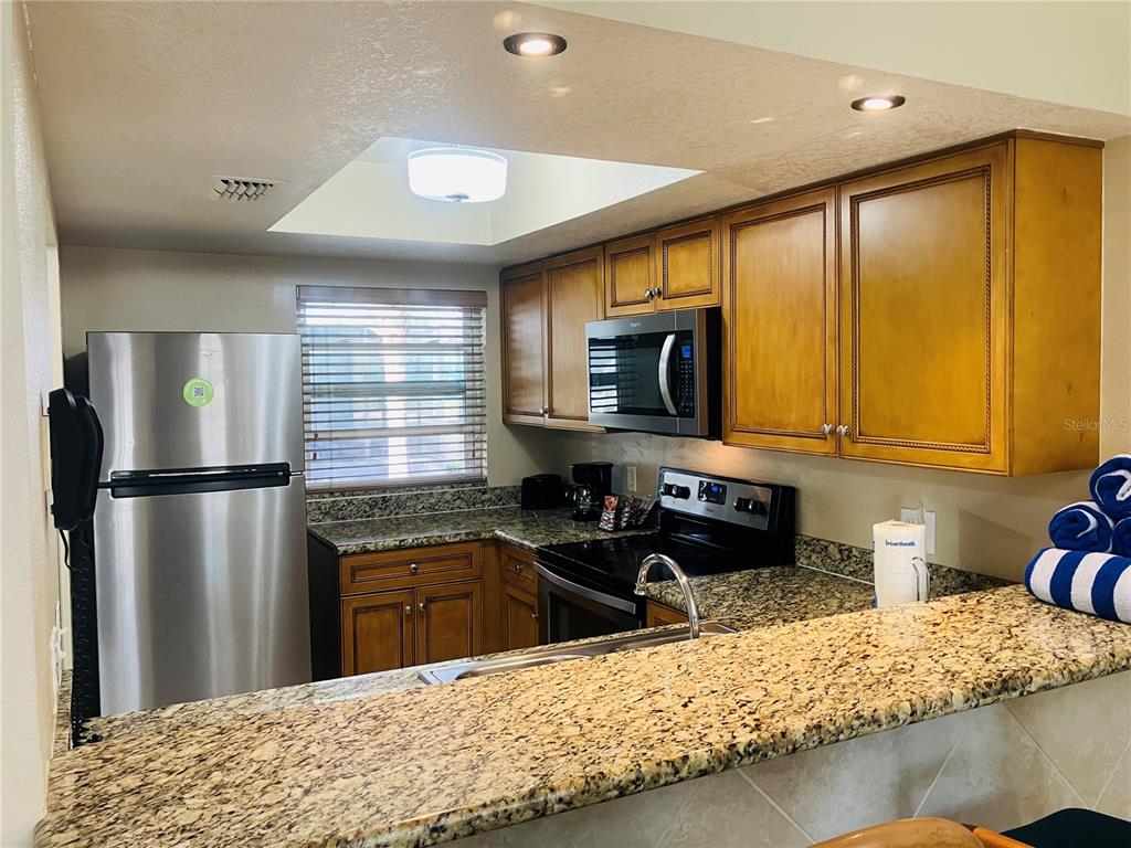 A kitchen features wood cabinets, granite countertops, stainless steel appliances, and a skylight — 1021 BASEBALL AND BOARDWALK COURT, KISSIMMEE, FL