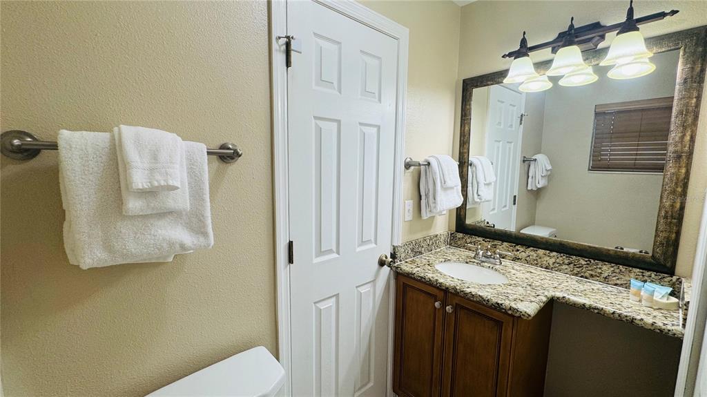 A bathroom features a granite vanity, a framed mirror, and white towels on wall racks — 1021 BASEBALL AND BOARDWALK COURT, KISSIMMEE, FL