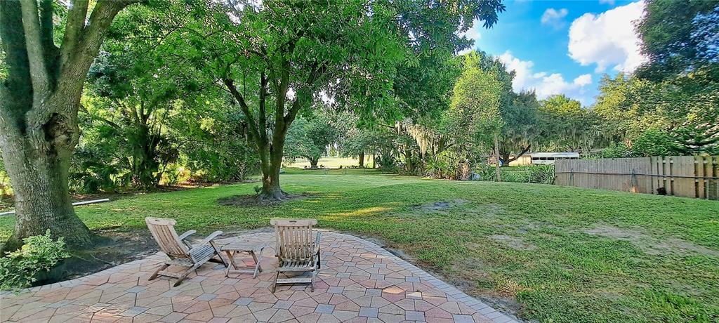 A paved patio with two wooden chairs sits in a grassy backyard shaded by trees — 3017 BAY LAKE ROAD, ORLANDO, FL