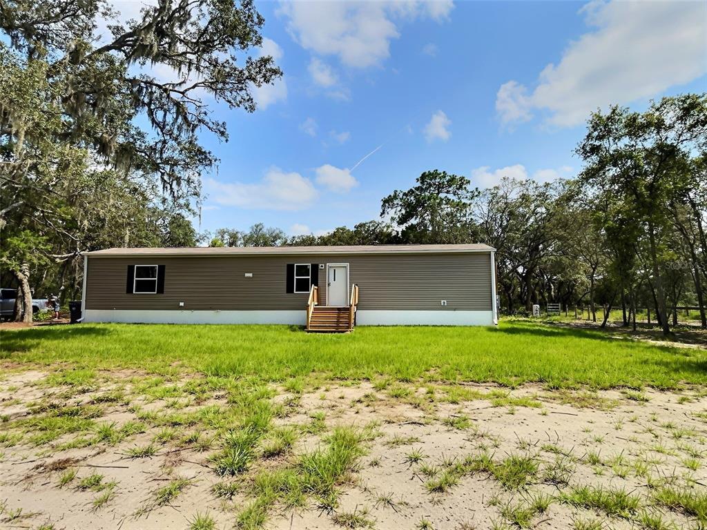A single-story manufactured home with brown siding and a wooden staircase sits on a grassy lot — 13354 TYRONE STREET, HUDSON, FL