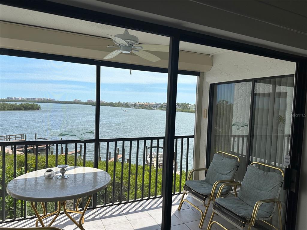 A screened-in balcony features a round table, two chairs, a ceiling fan, and water views — 4835 BONITA BEACH ROAD UNIT 203, BONITA SPRINGS, FL