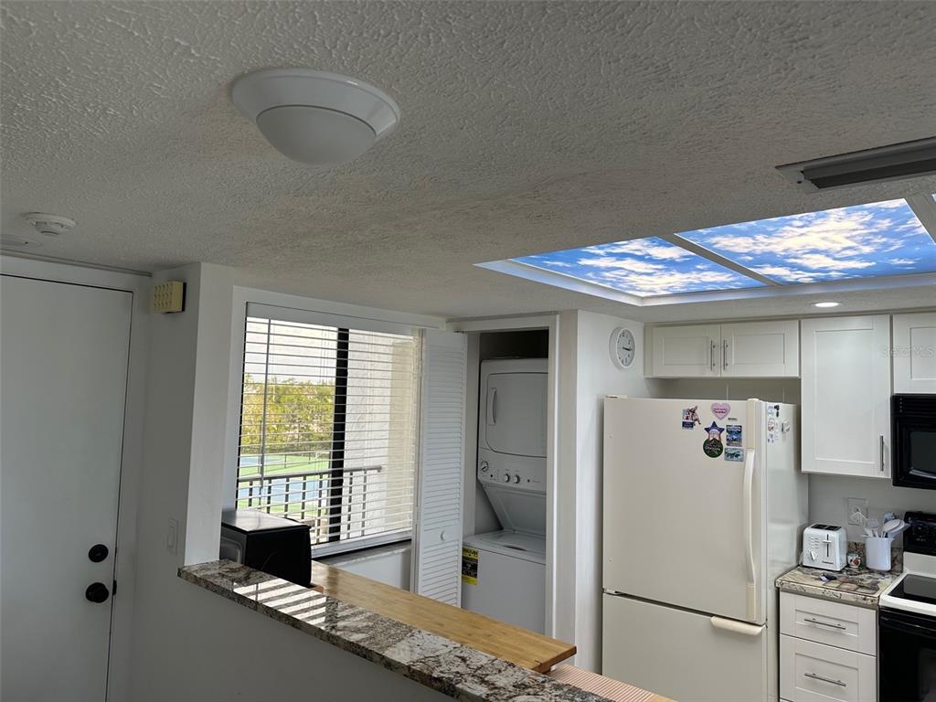A kitchen features white cabinets, a granite countertop, a stacked washer-dryer, and a skylight — 4835 BONITA BEACH ROAD UNIT 203, BONITA SPRINGS, FL