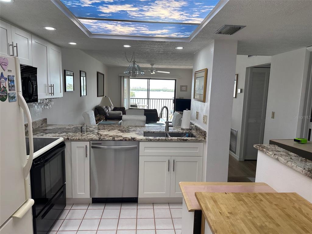 A kitchen with white cabinets and granite countertops overlooks a living area with water views — 4835 BONITA BEACH ROAD UNIT 203, BONITA SPRINGS, FL